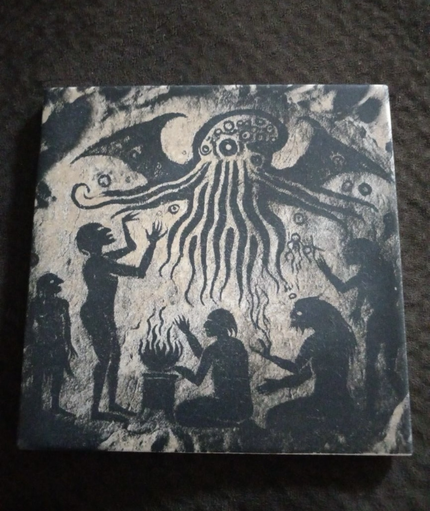 Stone-look tile of silhouettes around a fire with a tentacled creature overhead